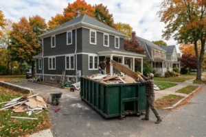 Contractor loading renovation debris into a residential dumpster outside a Massachusetts home during a remodeling project using a professional South Shore dumpster rental service.